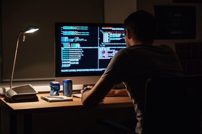 Back view of modern programmer sitting and writing code in dark room-1